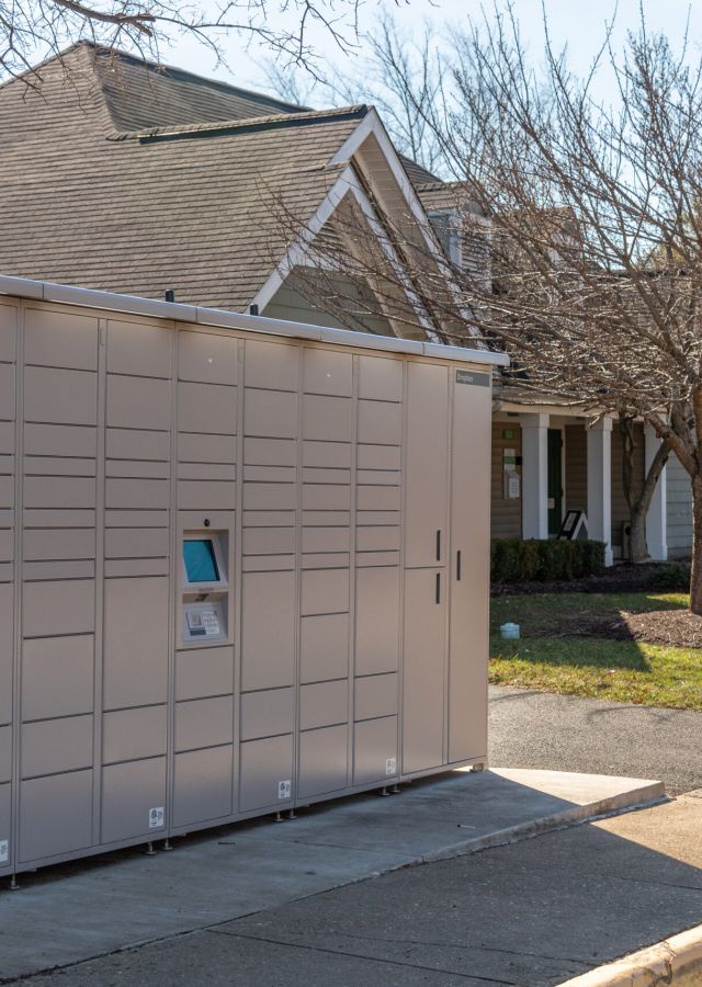 An Amazon Hub locker stands on a sidewalk in front of residential buildings and leafless trees.