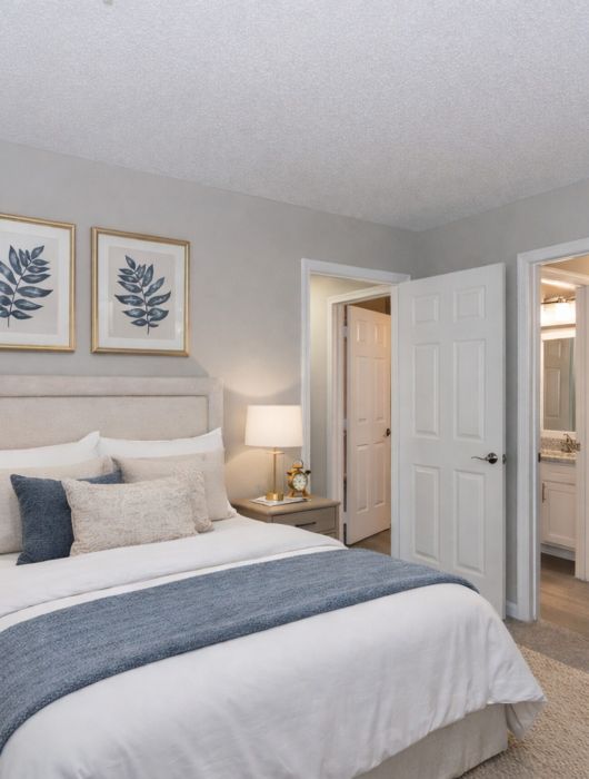 Modern bedroom with a neatly made bed, bedside tables, lamps, and two framed leaf prints on the wall.
