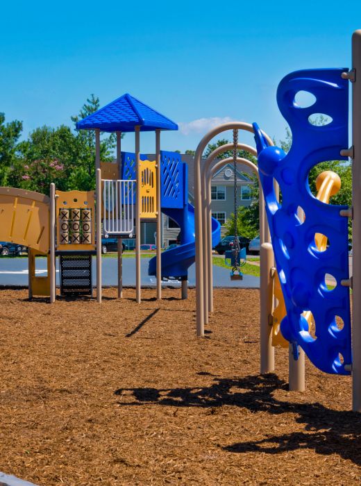 A colorful playground with slides and climbing structures on a mulch surface under a clear, sunny sky.